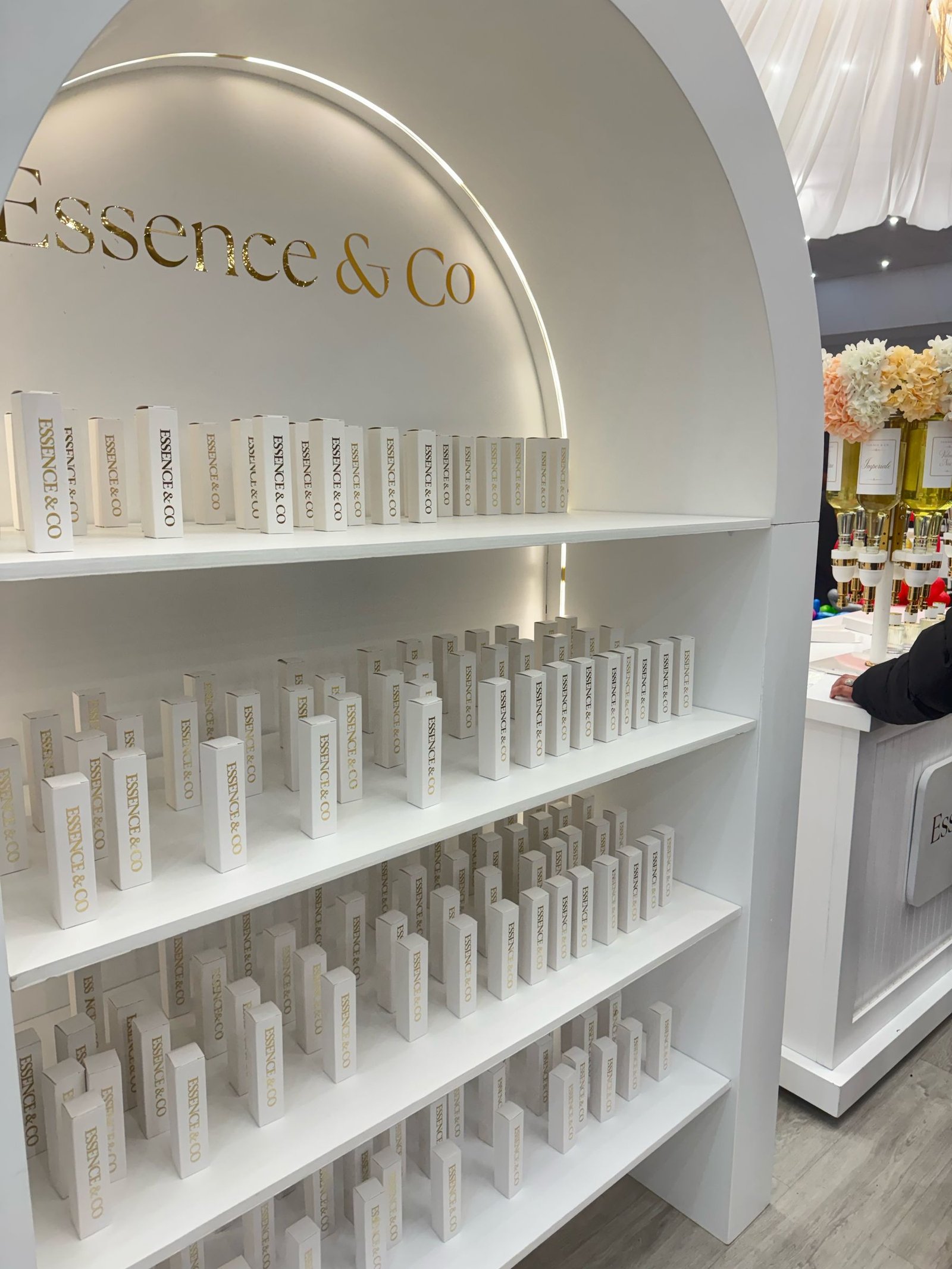 Essence & Co. arched display wall in gold lettering, lined with rows of custom-labelled perfume bottles