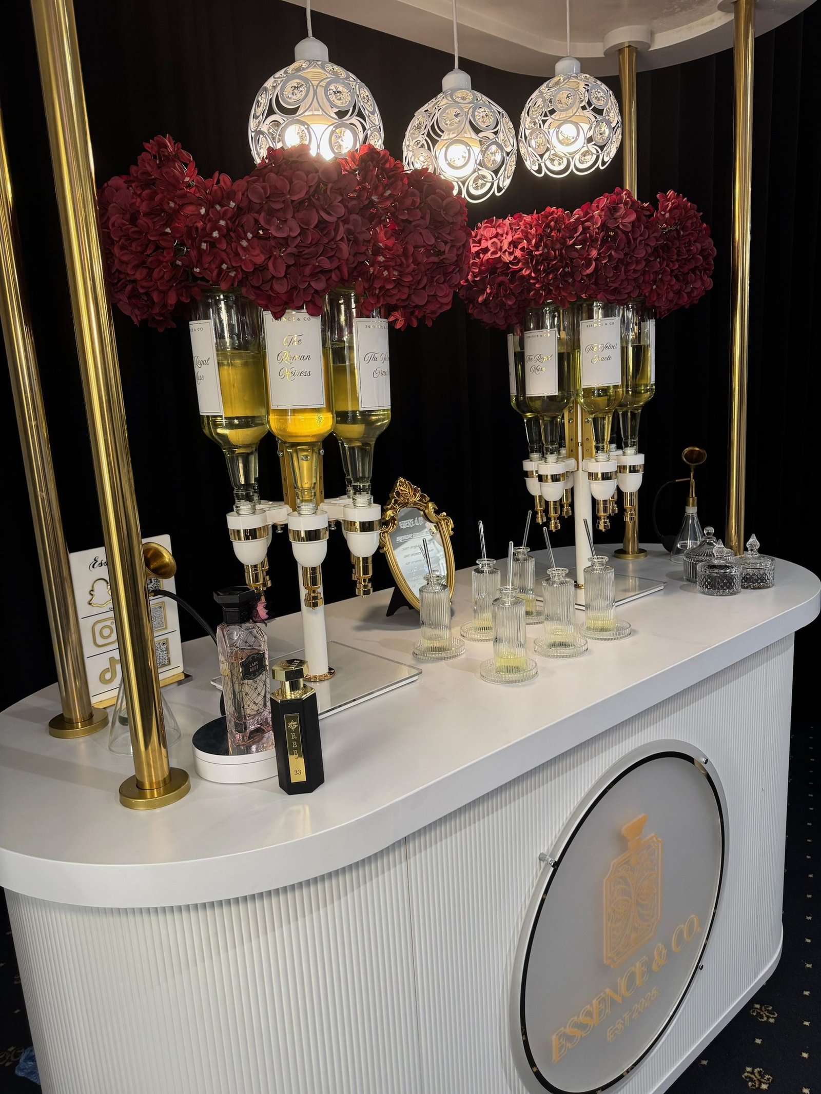 Essence & Co. perfume bar with gold dispensers, deep red hydrangeas and illuminated pendant lighting