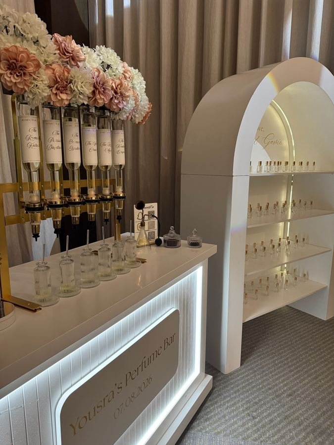 Personalised wedding perfume bar with illuminated signage, blush florals and an arched bottle display