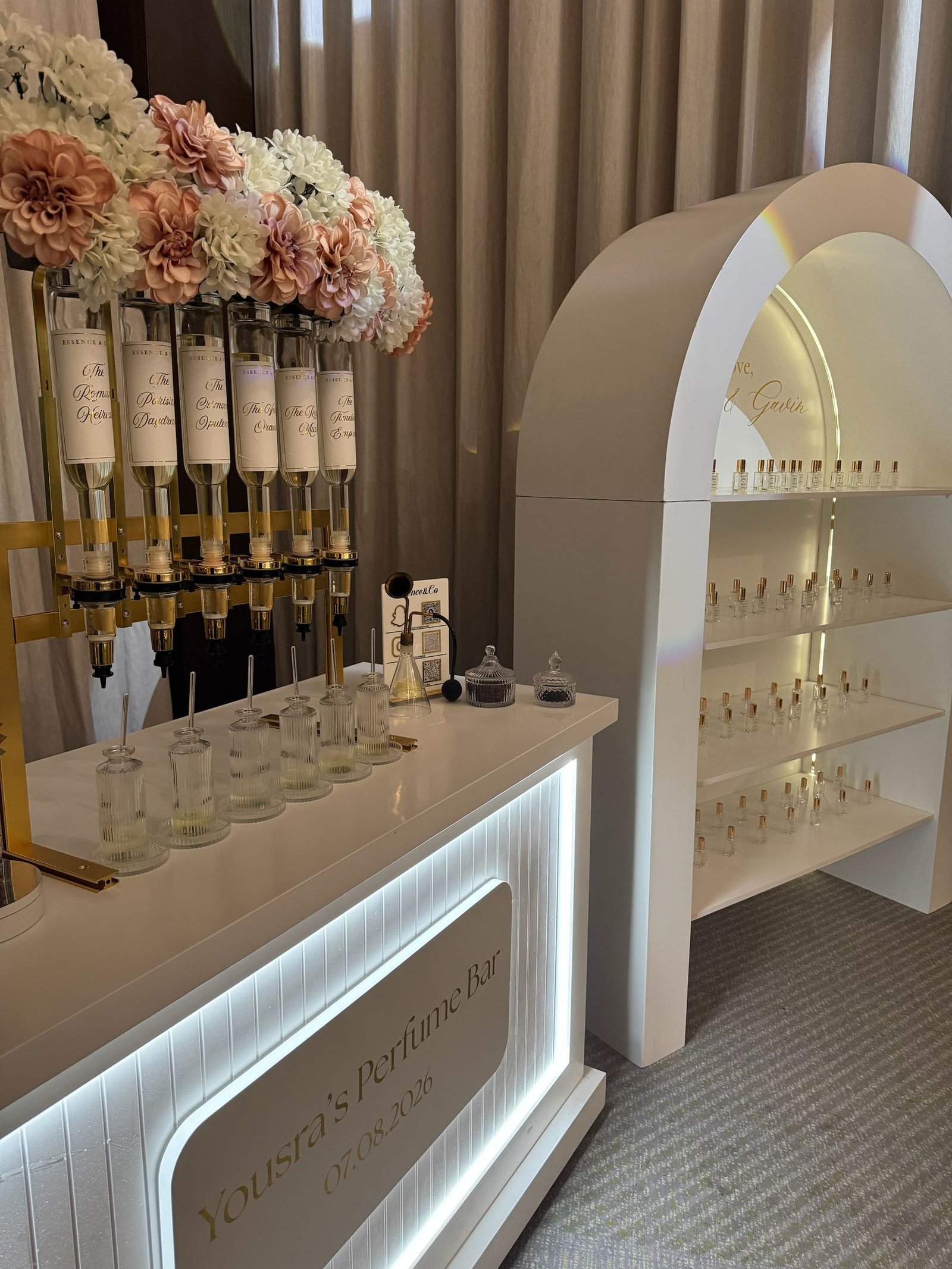 Personalised wedding perfume bar with illuminated signage, blush florals and an arched bottle display