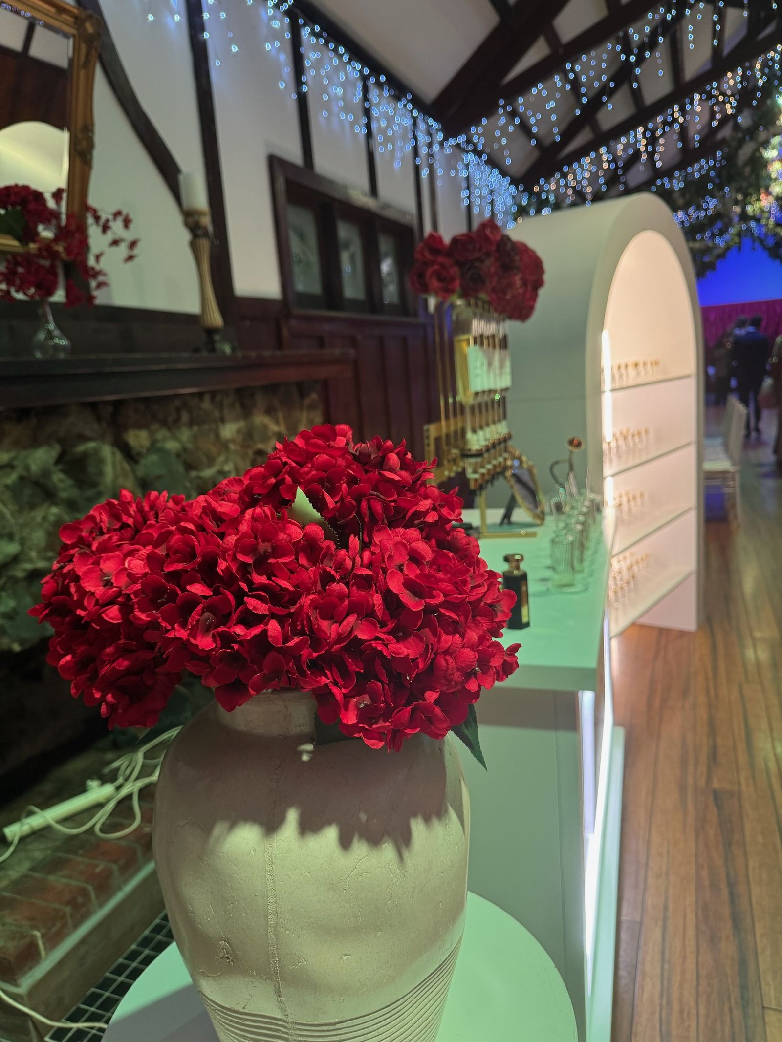 Perfume bar styled at a Melbourne wedding venue with red florals and fairy-lit ceiling beams